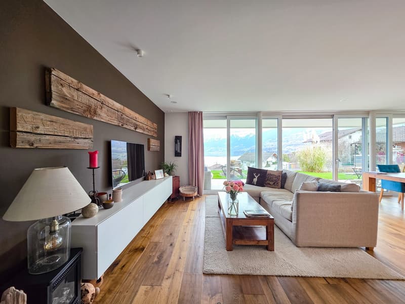 modern living room with wooden floor, large windows, couch, coffee table, TV, lamp, rug, wooden shelves, decorative items