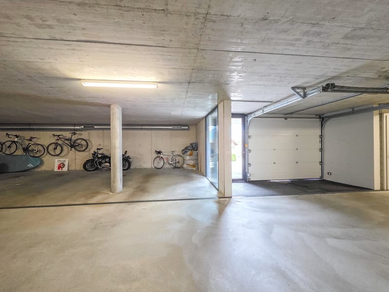 underground parking lot, bicycles, motorcycles, white garage doors, concrete walls, ceiling lights
