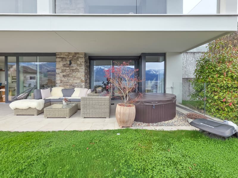 Outdoor patio with a sofa set, coffee table, hot tub, potted plant, and a grassy lawn