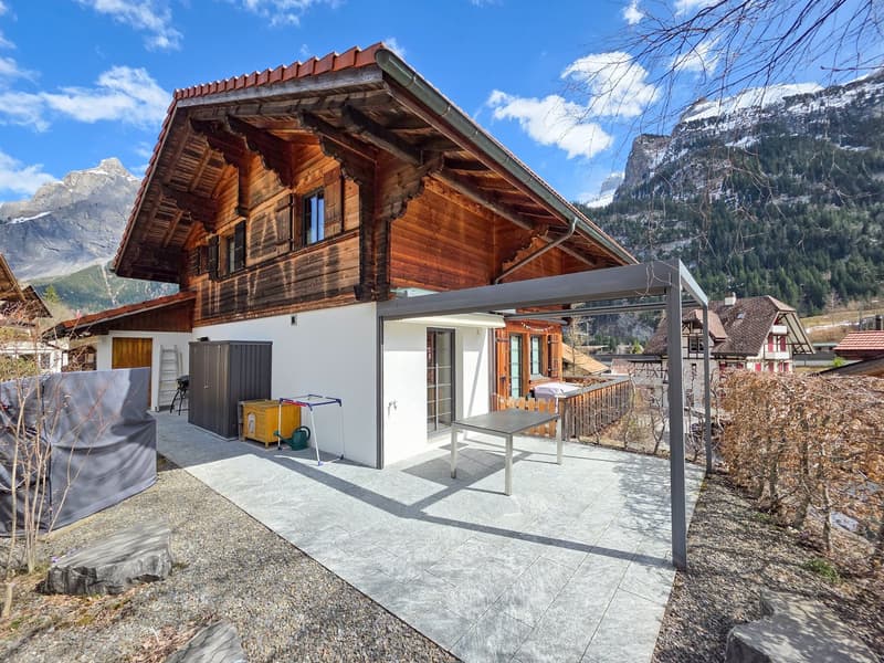 wooden chalet, red roof, white walls, large terrace, table, storage box, covered area, mountains in the background