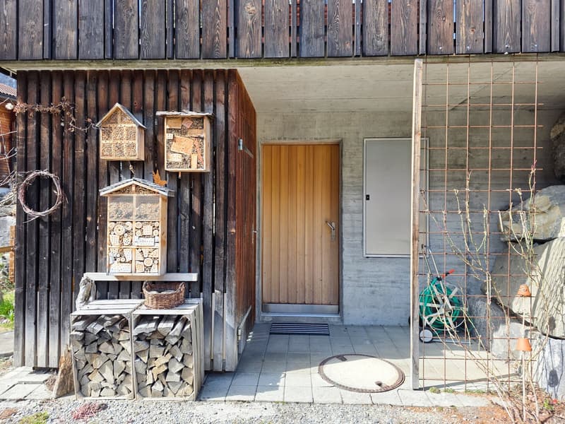 wooden exterior, wooden door, wooden shelves with baskets, logs, birdhouses, concrete floor, metal gate