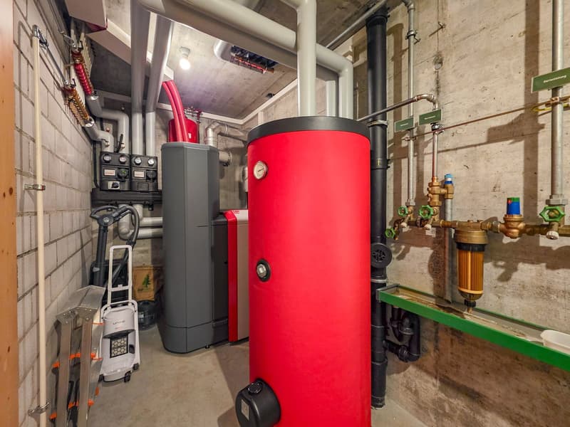 Utility room with a red water heater, a gray gas boiler, and various pipes and valves.