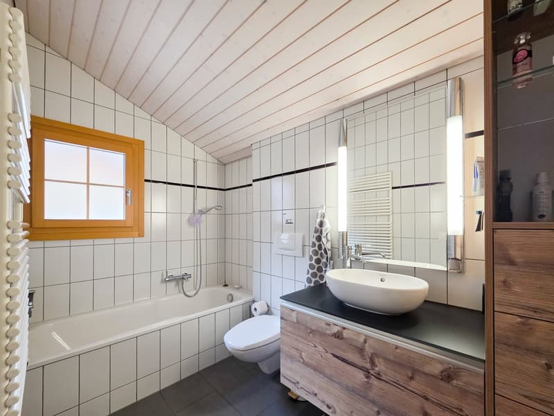 Bathroom with white tiles, bathtub, toilet, sink, mirror, wooden cabinet, wooden ceiling