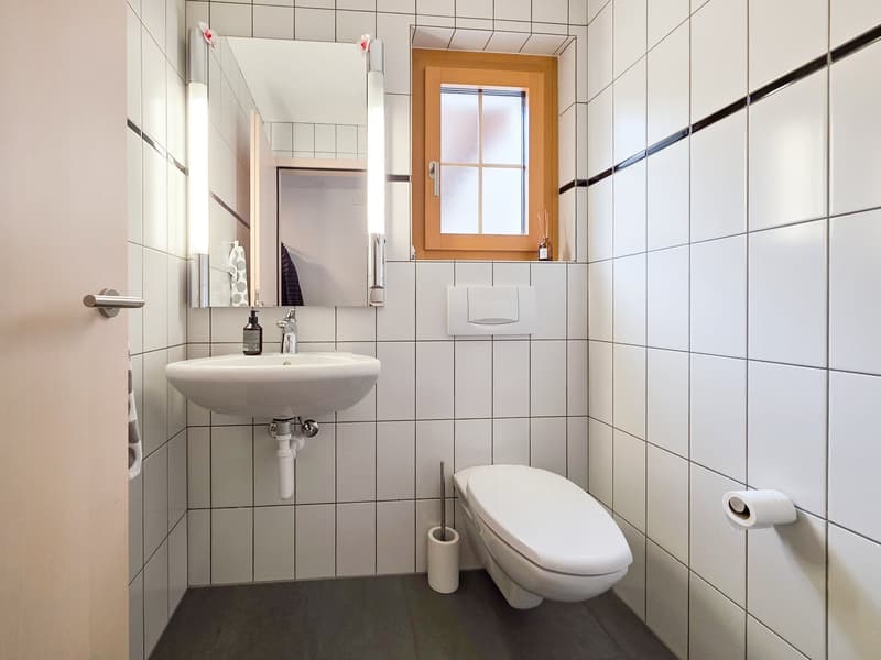 small bathroom with white tiles, sink, toilet, mirror, window, toilet paper holder