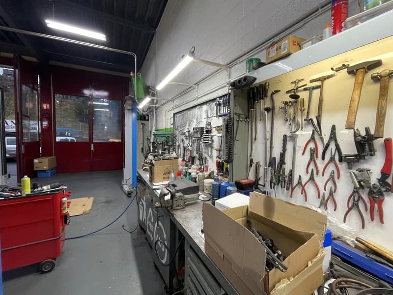 Industrial workshop with a range of tools and equipment on the wall, boxes and containers on the floor, a workbench with various tools and storage cabinets