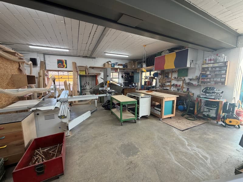 large workshop room with multiple wooden workbenches, equipment, metal shelves, and tools