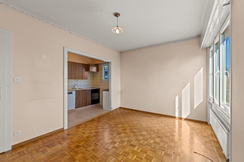 Empty room with wooden floor, white walls, large windows, kitchen with sink, dishwasher, and oven