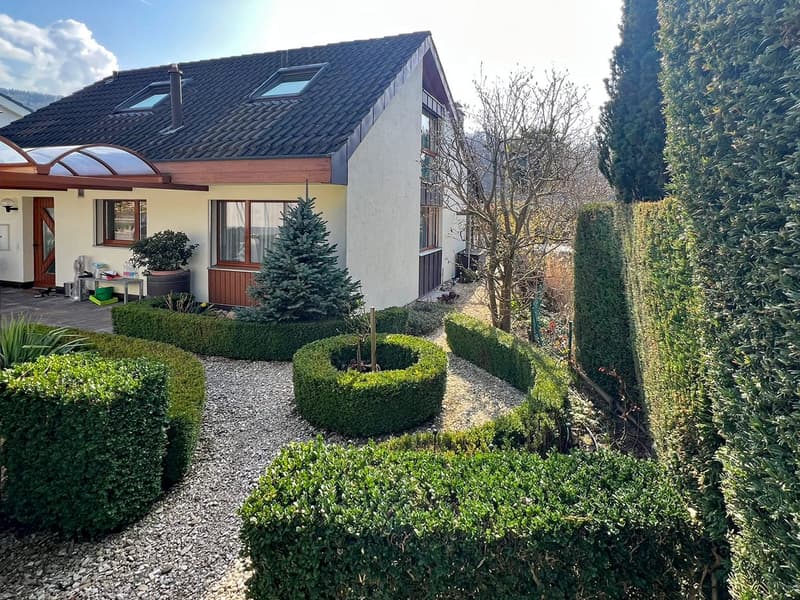 Detached house, black roof, white walls, two windows, brown door, small porch, two skylights, gravel pathway, hedges, potted plant, Christmas tree, small table with items