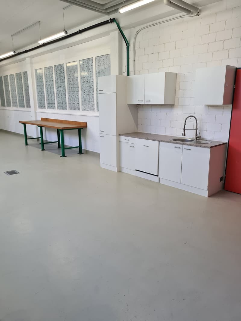 A kitchen with white cabinetry, gray countertops, a wooden work table, white brick walls, overhead fluorescent lighting, and a sink with a faucet.