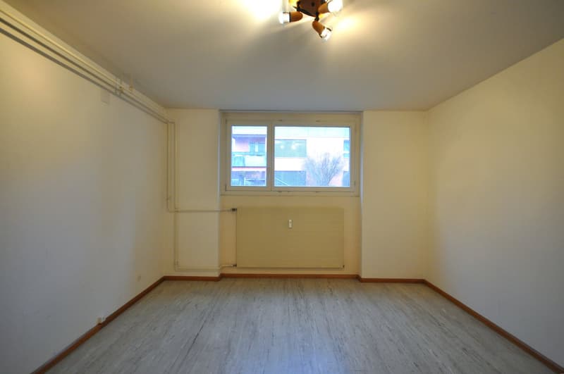 An empty room with white walls, wooden floor, a large window, and a radiator.
