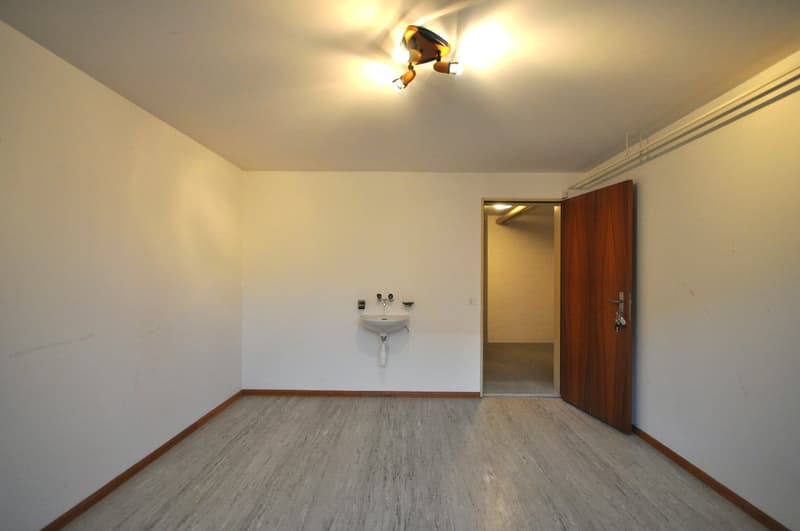 Empty room with white walls, wooden door, white sink, and gray floor