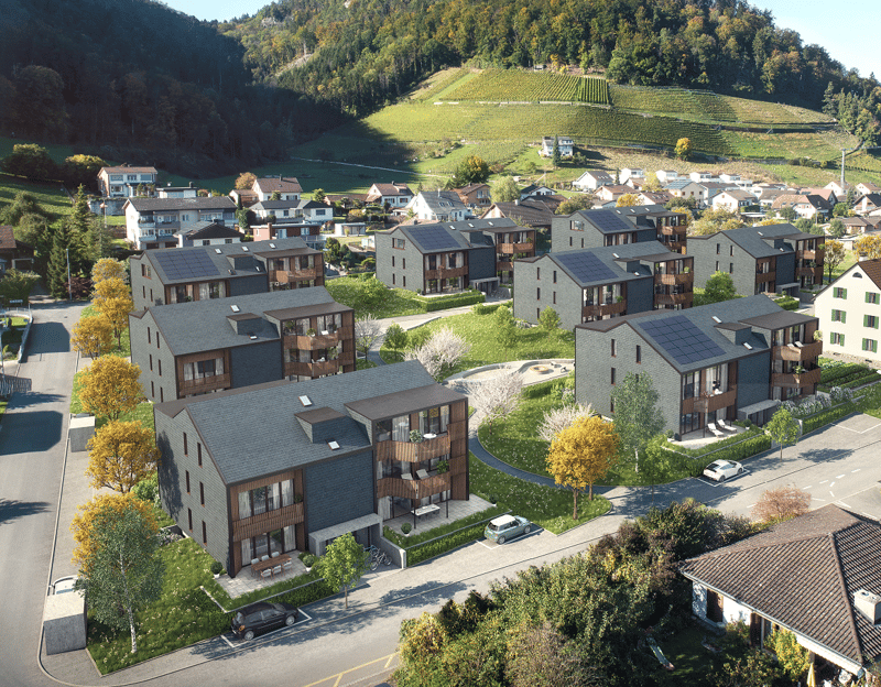 Aerial view of a residential area with multi-story apartment buildings, surrounded by lush greenery and vineyards on the hills in the background.