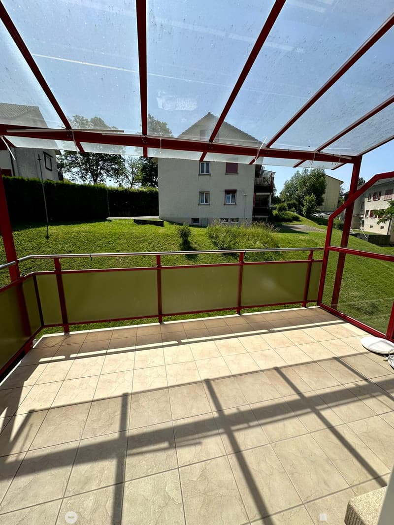 covered terrace with tiled floor, transparent glass roof, metal railings, green grass lawn in background