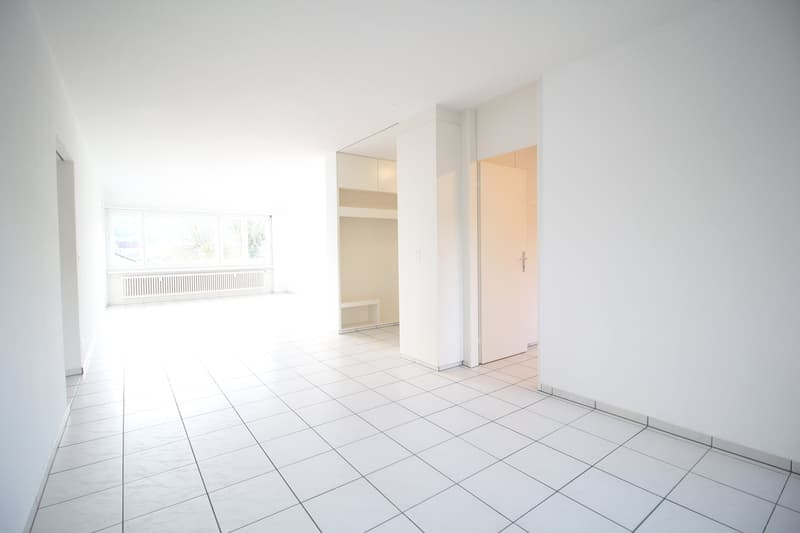 Empty room with white walls, white tiled floor, large window, and a small bench.