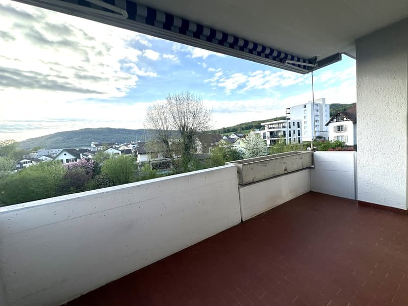 Balcony with white walls, red floor, white ceiling, white railing, concrete planter, blue and white striped awning, view of the city
