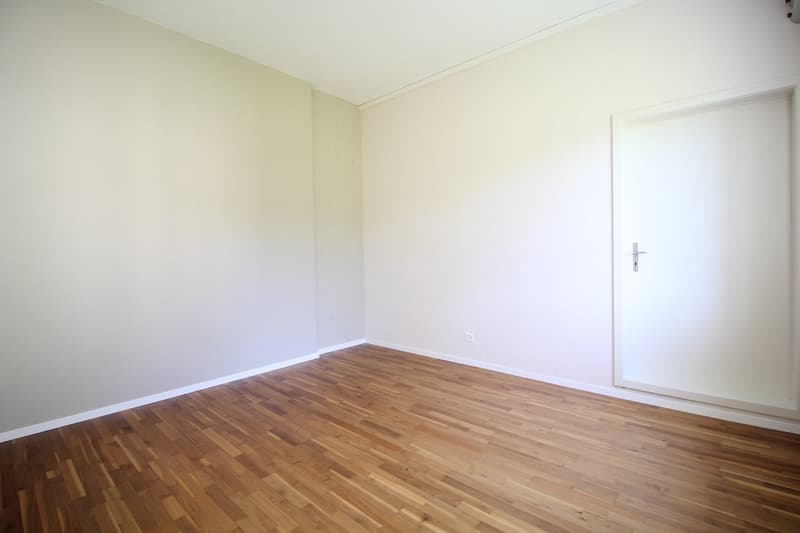 Completely empty room with white walls, wooden floor, and a white door.