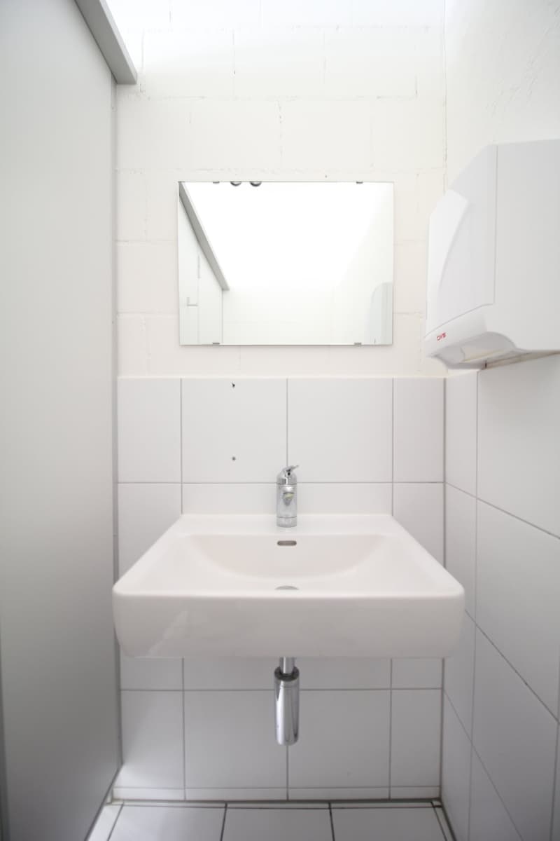 Bathroom with white sink, faucet, mirror, and hand dryer on tiled walls.