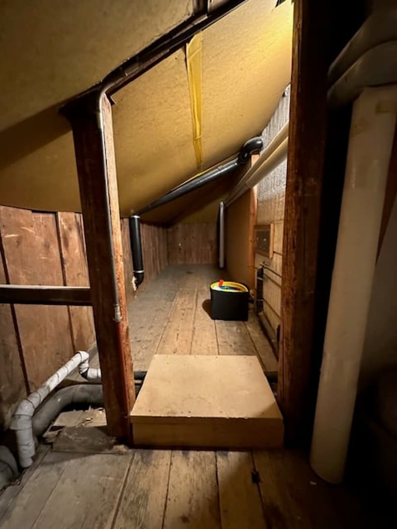 attic room with wooden floor, wooden walls, pipes, wooden step, black storage box