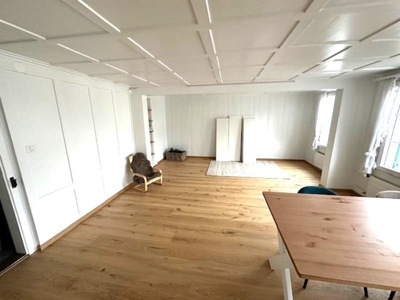 Empty room with wooden floor, white walls, white ceiling, wooden table, chair, rug, windows, doors