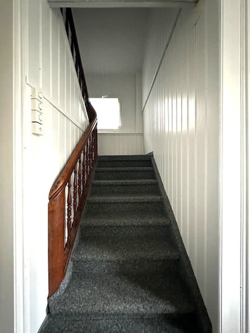 wooden handrail, carpeted steps, white walls, small window