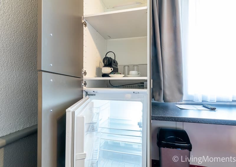 Open kitchen cabinet with kitchen appliances and utensils, refrigerator, countertop, and window