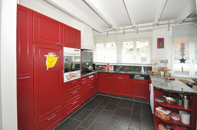 Modern kitchen with red cabinetry, granite countertops, integrated appliances, ample storage, and a breakfast nook.