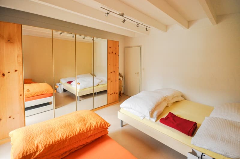 Three single beds, mirror, wooden wardrobe, white walls, beige floor