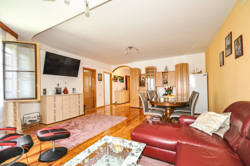 Spacious living room with hardwood floors, red leather sofa, wooden dining table and chairs, built-in cabinets, and a fireplace.