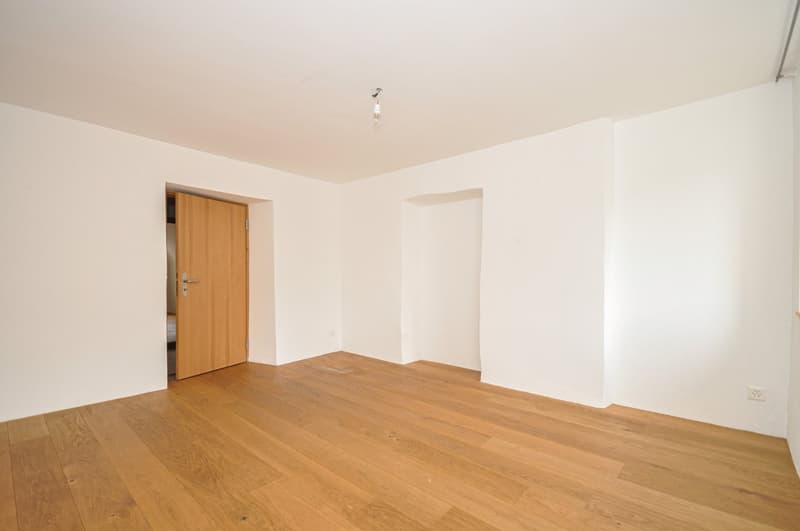 Empty room with white walls, wooden floor, and a wooden door.
