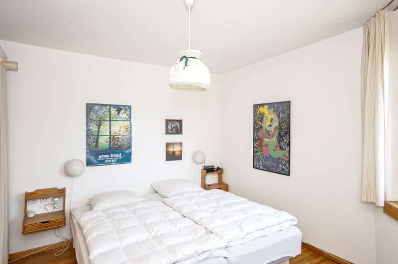 Bedroom with two single beds, hanging lamps, pictures on the wall, wooden nightstand, wooden wall outlet and plug