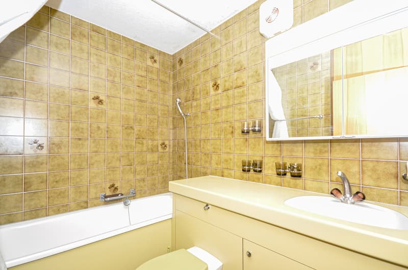 Bathroom with tiled walls, bathtub, shower head, sink, mirror, wooden cabinets