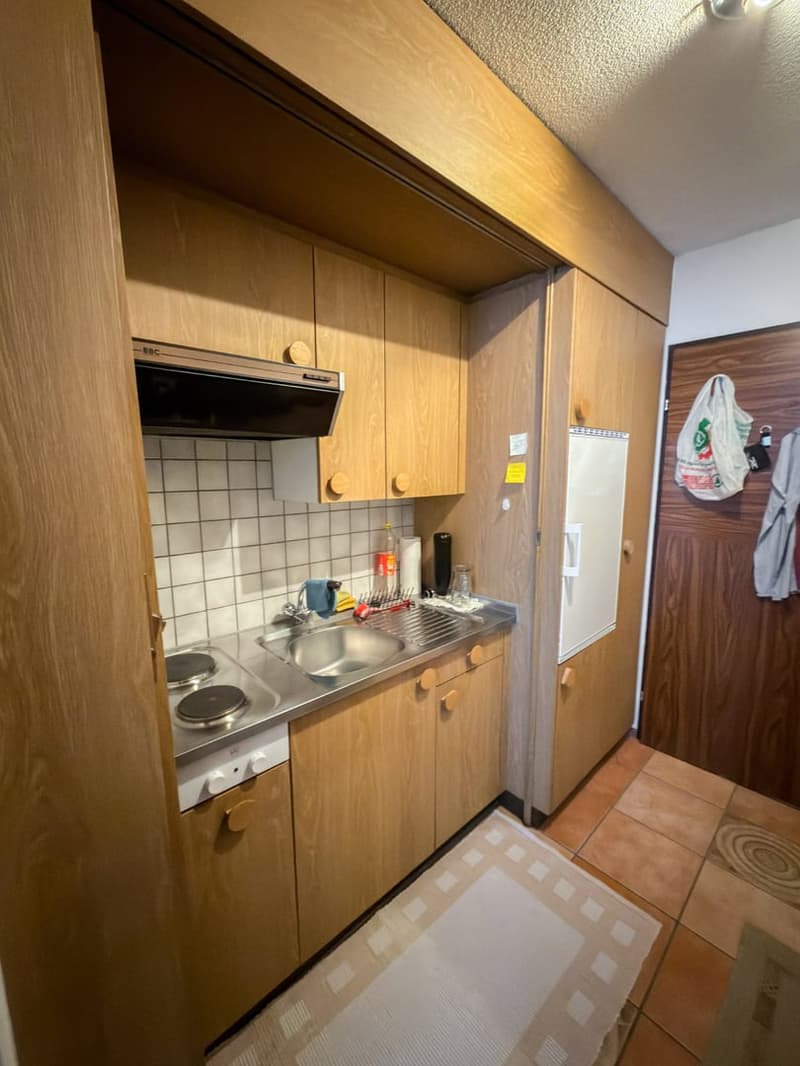 Wooden cabinets, tiled backsplash, stainless steel countertop, sink, electric stove, and a refrigerator