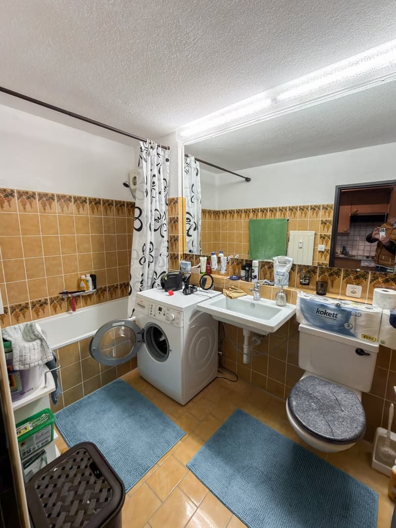 white walls, tiled floor, washing machine, bathtub, sink, toilet, blue rugs, mirror, towels and toiletries