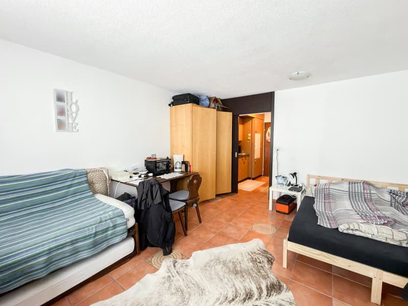 spacious room with two beds, wooden cabinets, desk, office chair, animal skin rug, white walls, and tiled floor