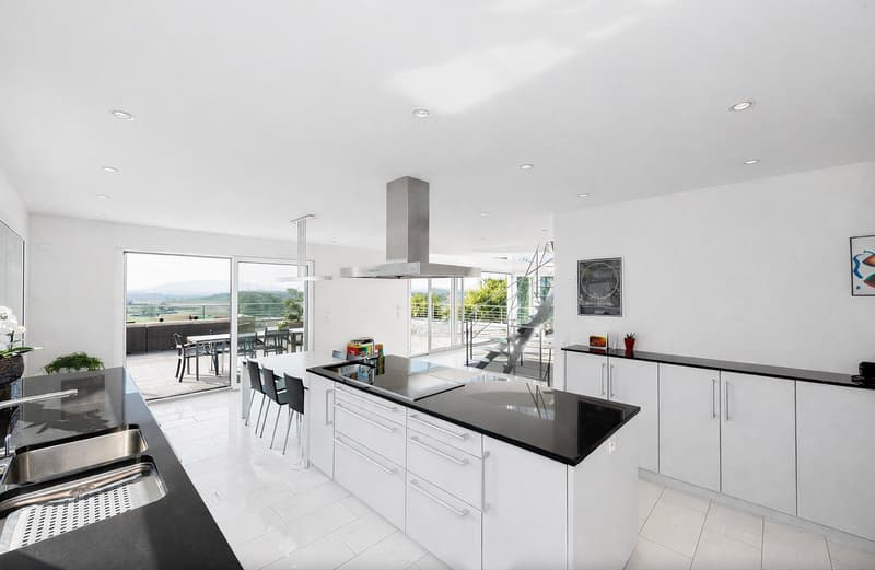 modern kitchen with white cabinets, black countertops, stainless steel appliances, large windows, balcony with outdoor dining area