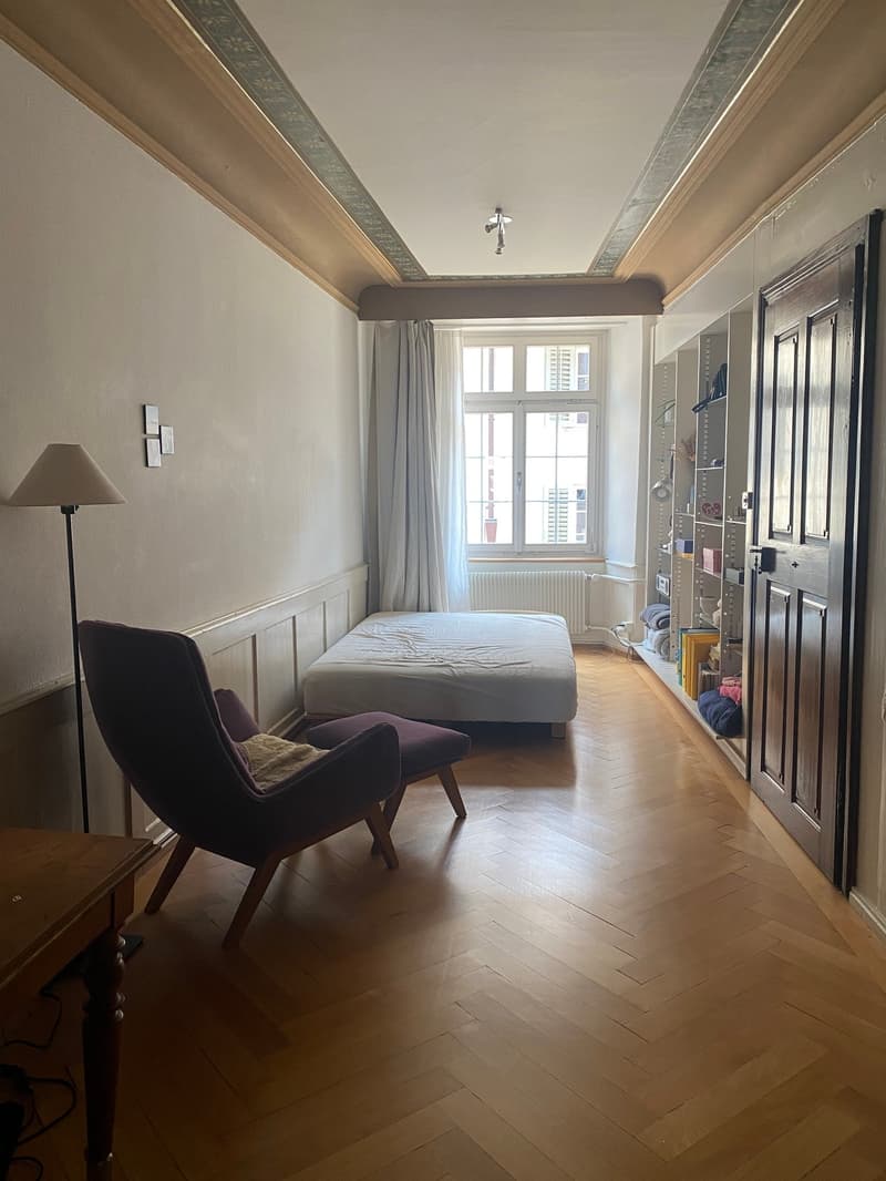 Empty room, wooden floor, double bed, chair, side table, large window with white curtains, radiator, lamp, open closet