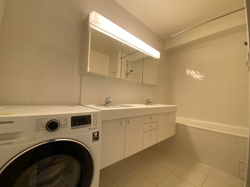 clean and modern bathroom with white washer, sink, mirror, bathtub, and tile floor