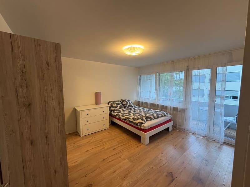 single bed with red and white sheets, a white dresser with drawers, a lamp, sliding doors leading to a balcony, parquet flooring, and a white ceiling with a round ceiling light