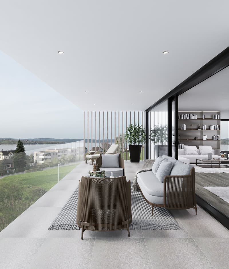 Spacious living room with large windows offering a scenic view, modern furniture including a sofa and armchairs, a coffee table, and shelving units on the wall. The room has a balcony or terrace overlooking the surrounding landscape.