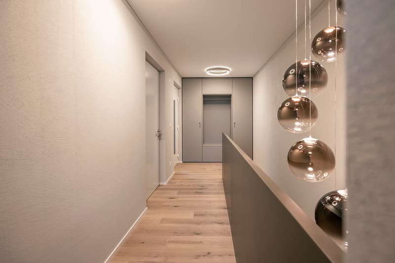 Spacious hallway with hardwood flooring, gray walls, built-in closets, and modern pendant lighting fixtures.