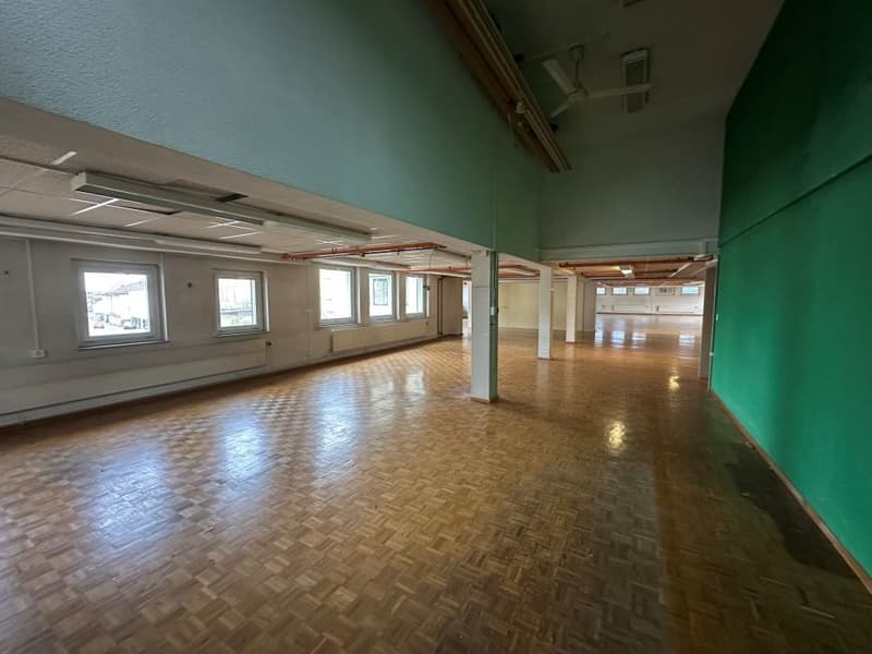 open space with large windows, wooden floor, exposed ceiling beams, ceiling mounted lamps