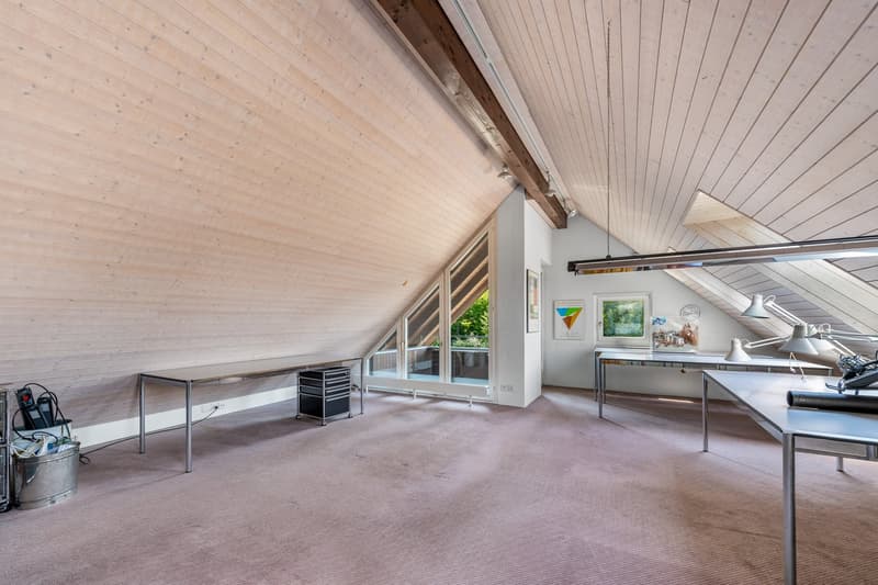 A room with carpeted floor, a table, office equipment, and windows leading to a balcony