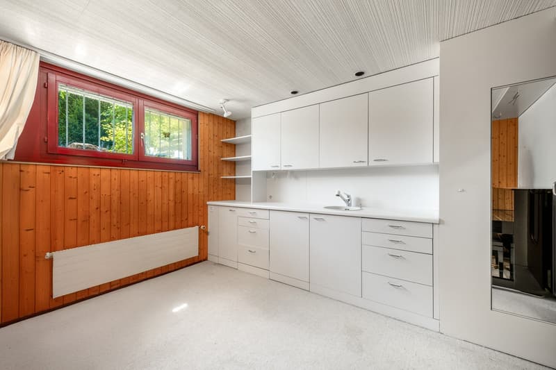 Small kitchen area with white cabinets, wooden floor, sink, window with red frame
