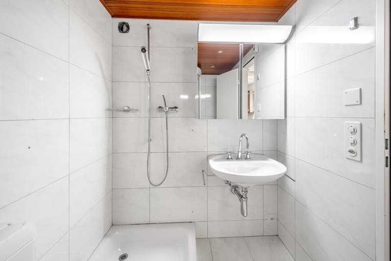 White tiled walls, white bathtub, shower head, white sink with mirror, toilet
