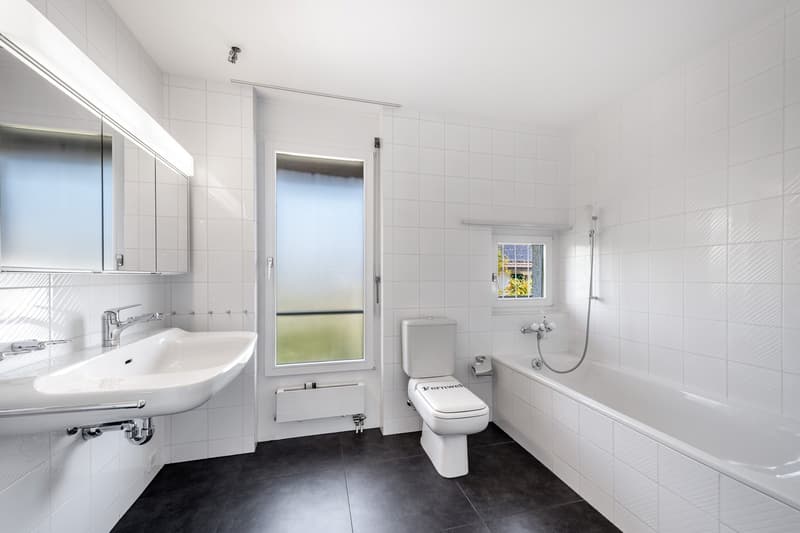 modern, minimalist bathroom with white tiles, bathtub, toilet, sink, and a window