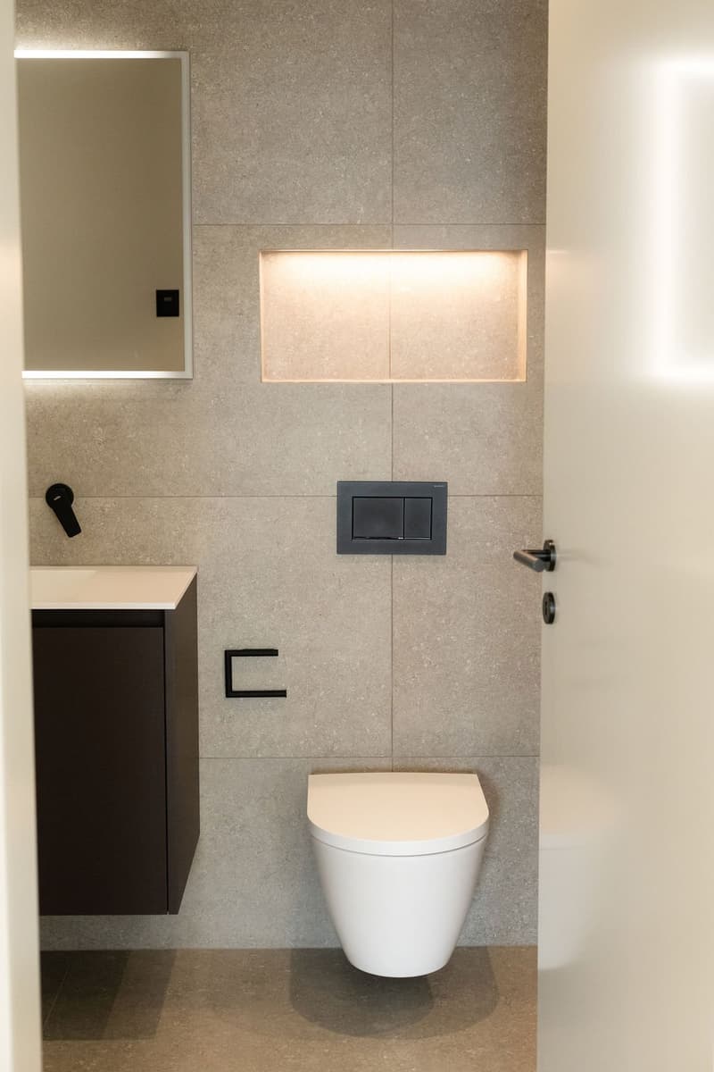 modern styled bathroom, with modern toilet, and brown wooden cabinet, with wall lighting, mirror