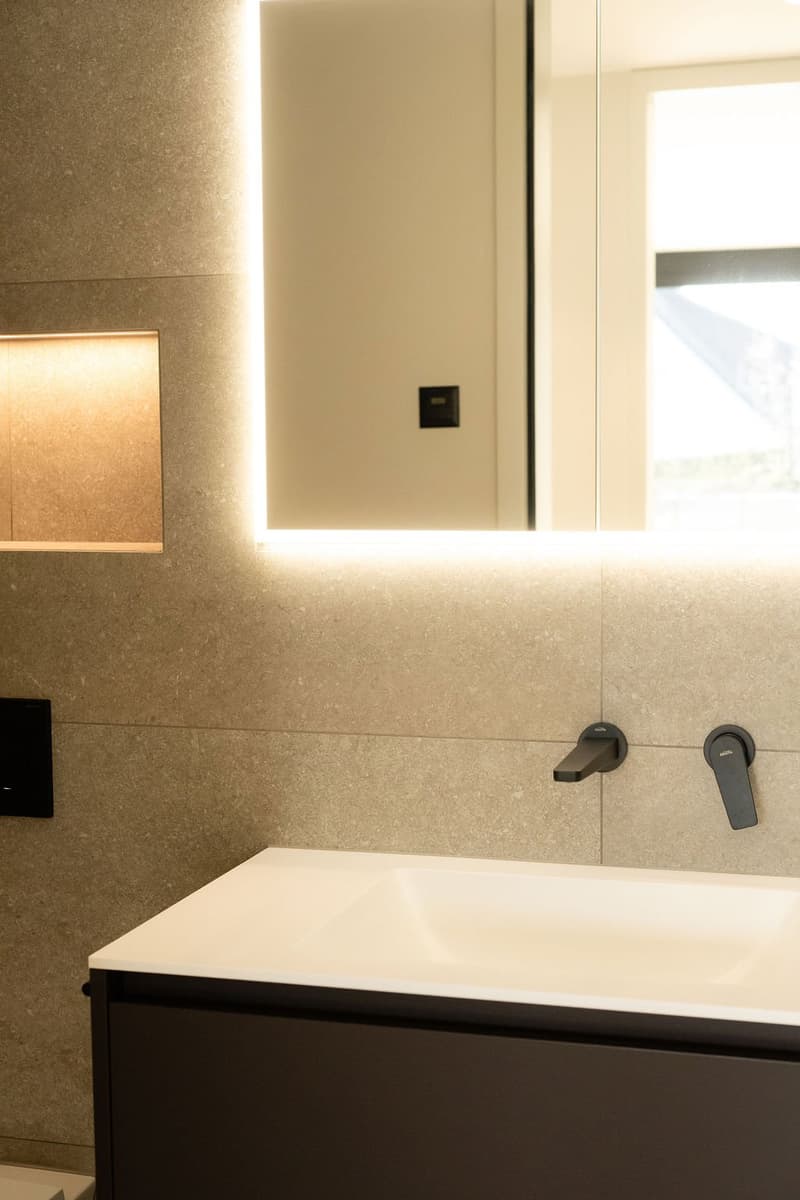 Bathroom: tiled walls, LED lighting, modern sink with black faucets, large mirror, light switches