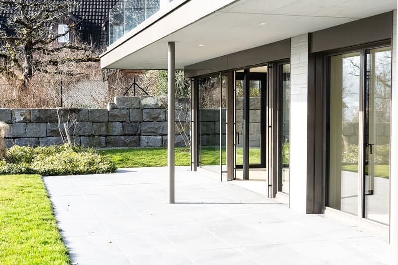 modern building with glass entrance doors, stone retaining wall, tiled path, lawn, and tree