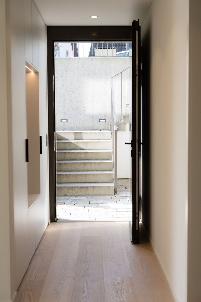 hallway, open entrance door, tiled floor, concrete staircase, wall-mounted lights