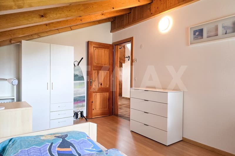 Bedroom with wooden ceiling, white walls, wooden door, white wardrobe, white dresser, bed with cat print cover, lamp, picture frame, ironing board